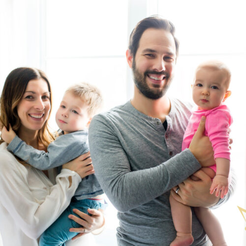 Portrait Of Young Family Relaxing Close To The Window With Baby